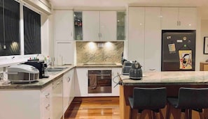 Eine moderne Küche mit weißen Schränken, einer Marmorarbeitsplatte und einem eingebauten Backofen. An der Kochinsel stehen zwei Stühle und ein Kühlschrank mit Magneten.