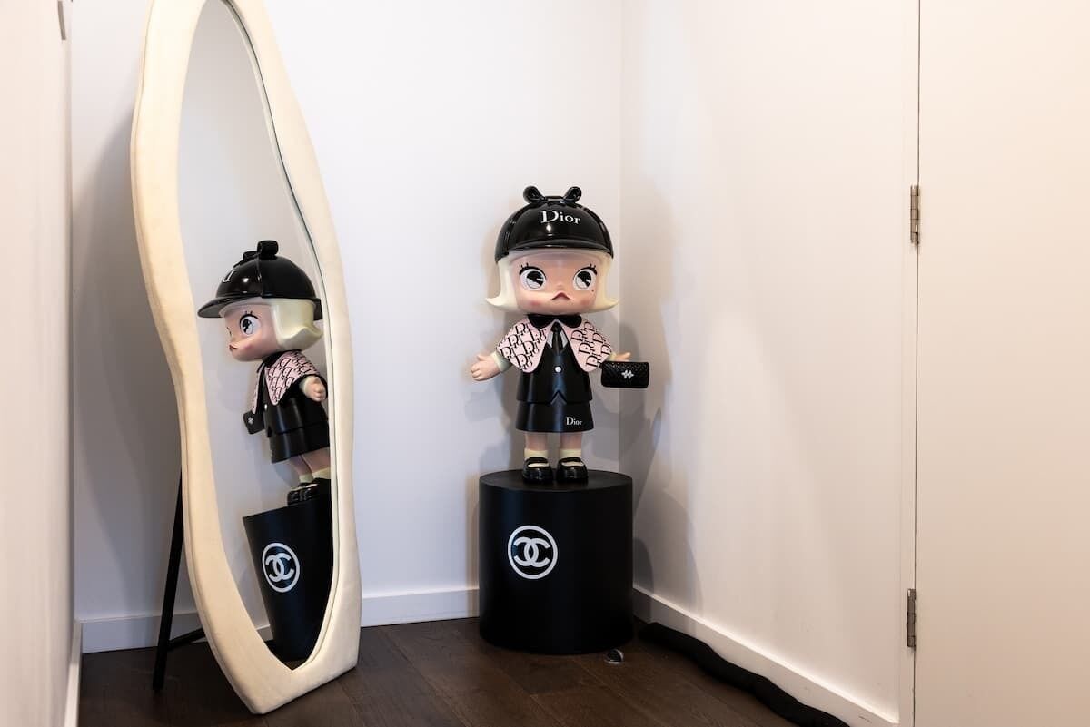 A doll on a black pedestal with a Chanel logo, standing next to a mirror with a Chanel logo.