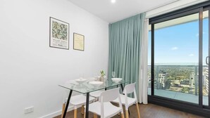 Ein moderner Essbereich mit einem Glastisch, weißen Stühlen und Blick auf die Stadt durch große Fenster.
