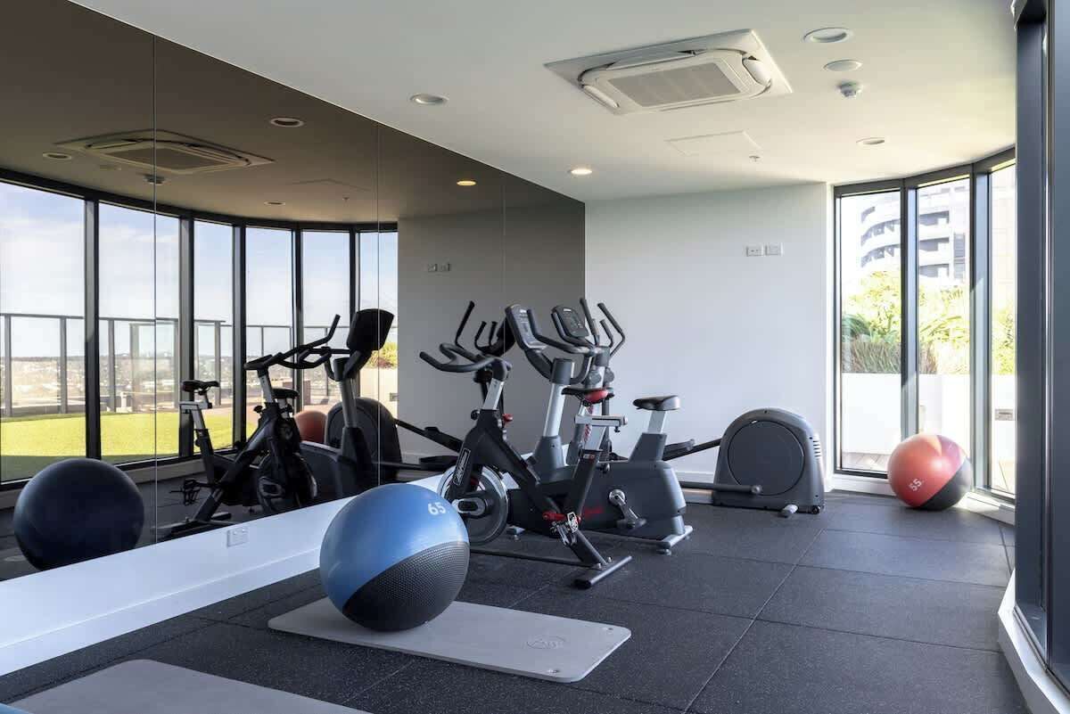 Une salle de sport moderne, équipée de matériel d’exercice, dotée de grandes fenêtres et offrant une vue sur l’extérieur.