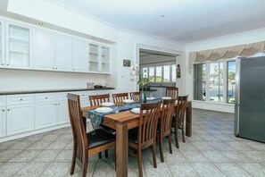 Cozinha espaçosa com armários brancos, mesa de jantar para seis pessoas e uma grande janela com vista para o exterior.