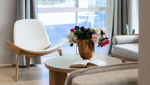 Un salon moderne avec un fauteuil blanc, une table basse ronde sur laquelle repose un livre, et un vase rempli de fleurs.