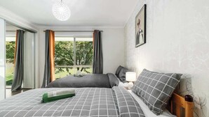 Une chambre à coucher avec un grand lit, une table de chevet avec une lampe et une fenêtre avec des rideaux.