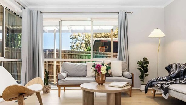 Un salon moderne avec un canapé, une table basse ronde et un fauteuil. Une grande fenêtre, ornée de rideaux, offre une vue sur l’extérieur.