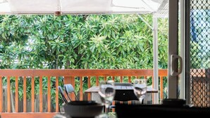 Un espace extérieur abrité, doté d’une rambarde en bois, d’une table et de chaises.