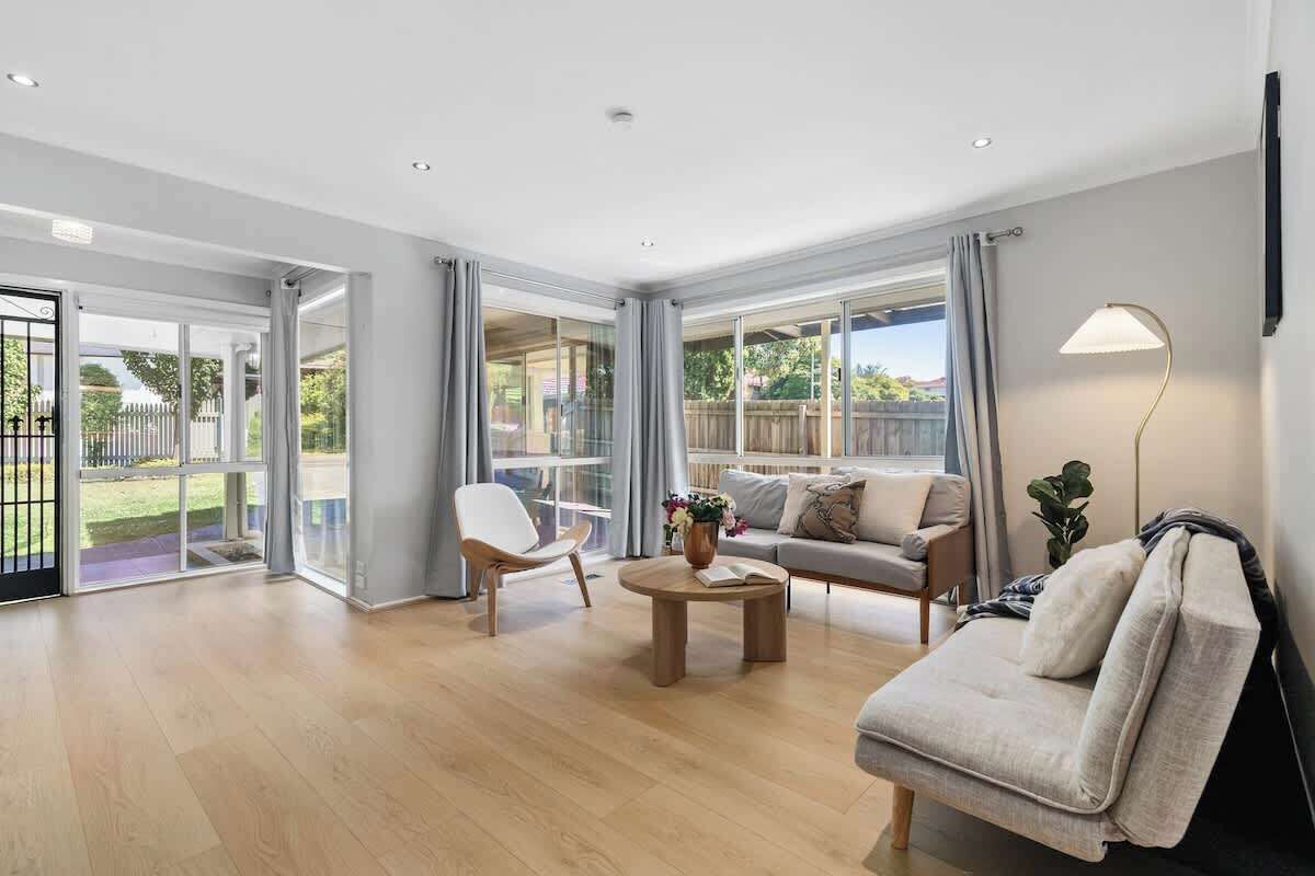 A spacious living room with a sofa, armchair, and coffee table, large windows, and a sliding glass door leading to a patio.