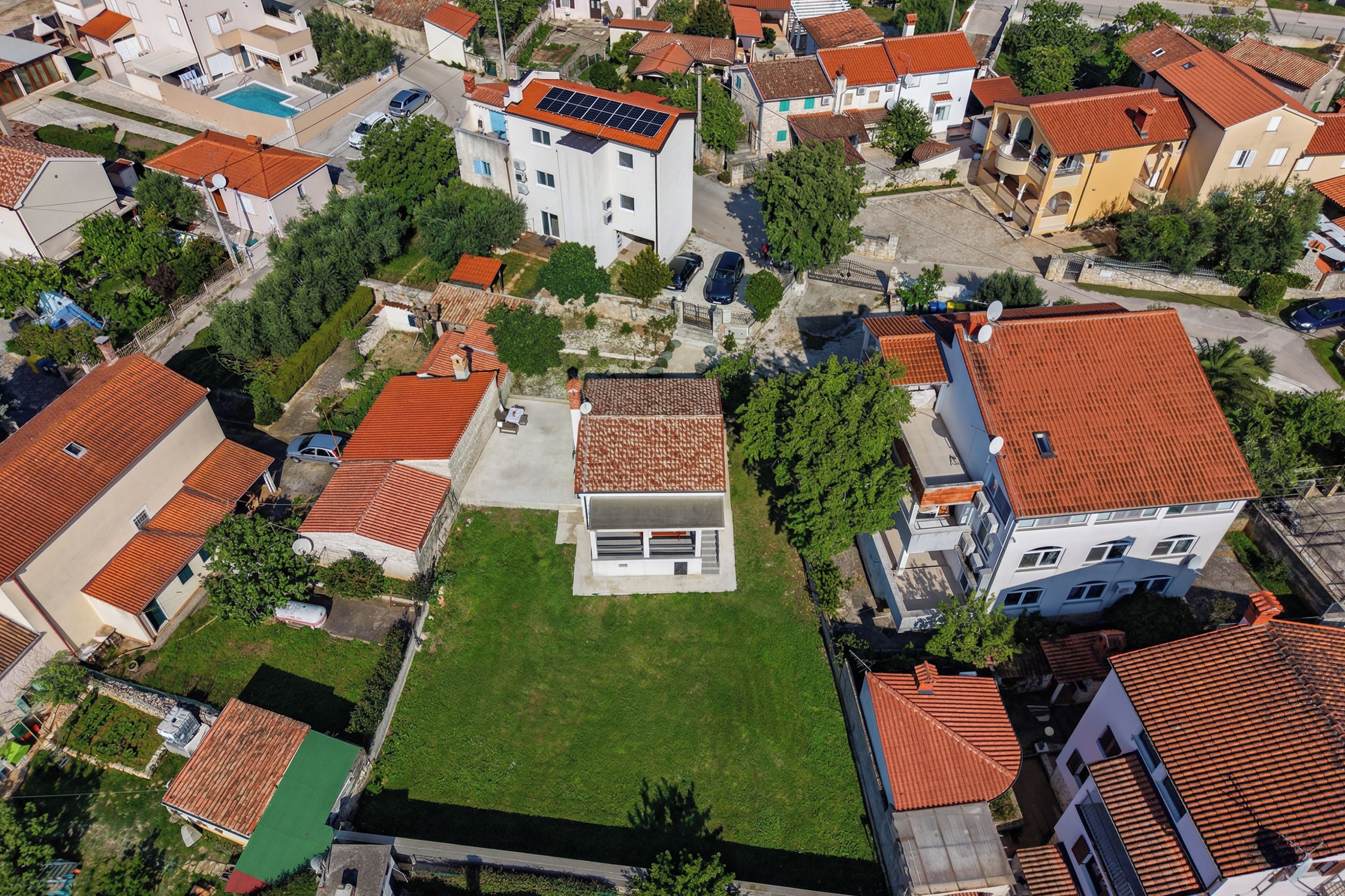Vue aérienne d’un quartier résidentiel avec des maisons, une piscine et une pelouse verdoyante.