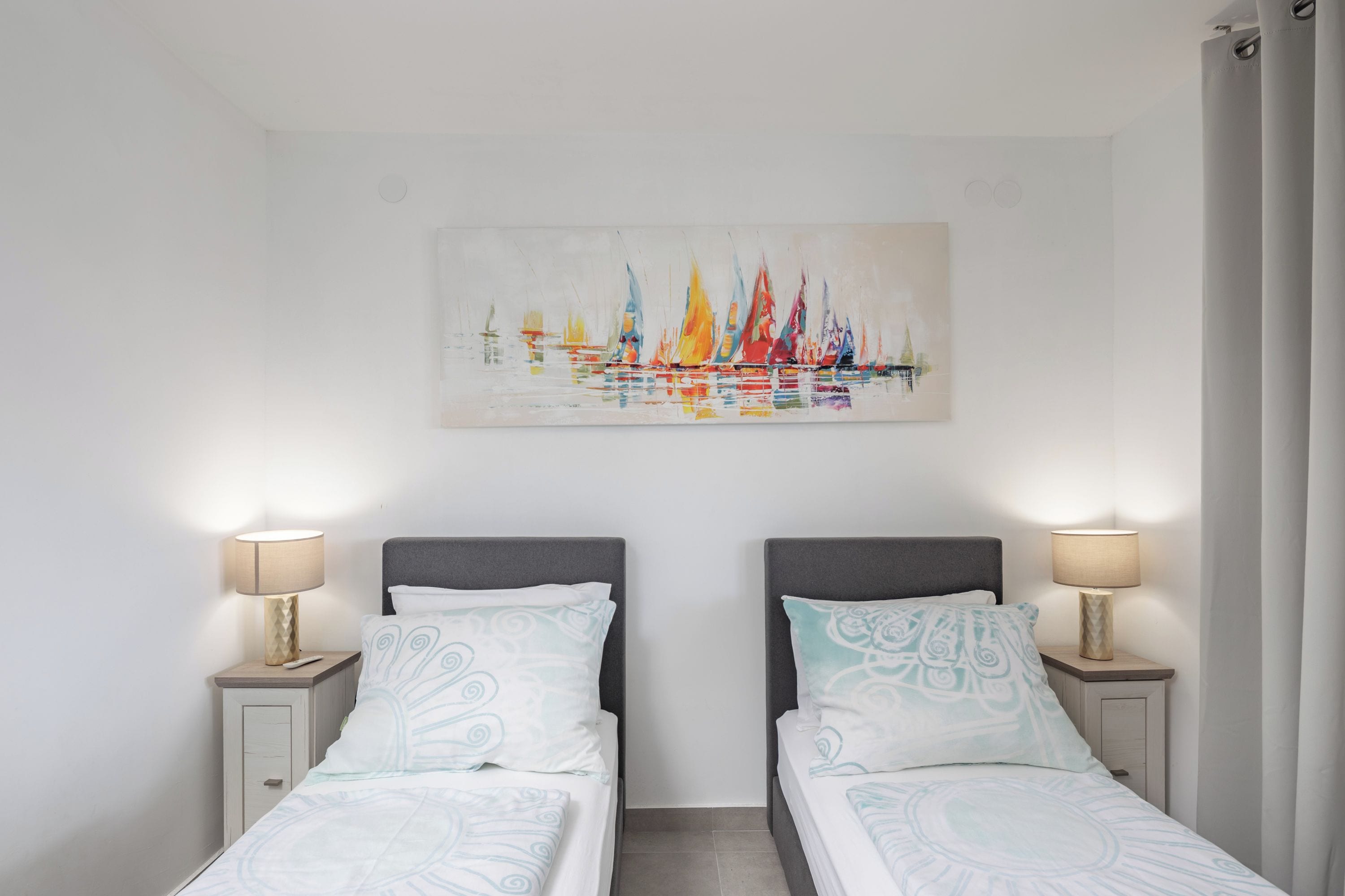 A hotel room with two beds, a painting of sailboats, and bedside lamps.