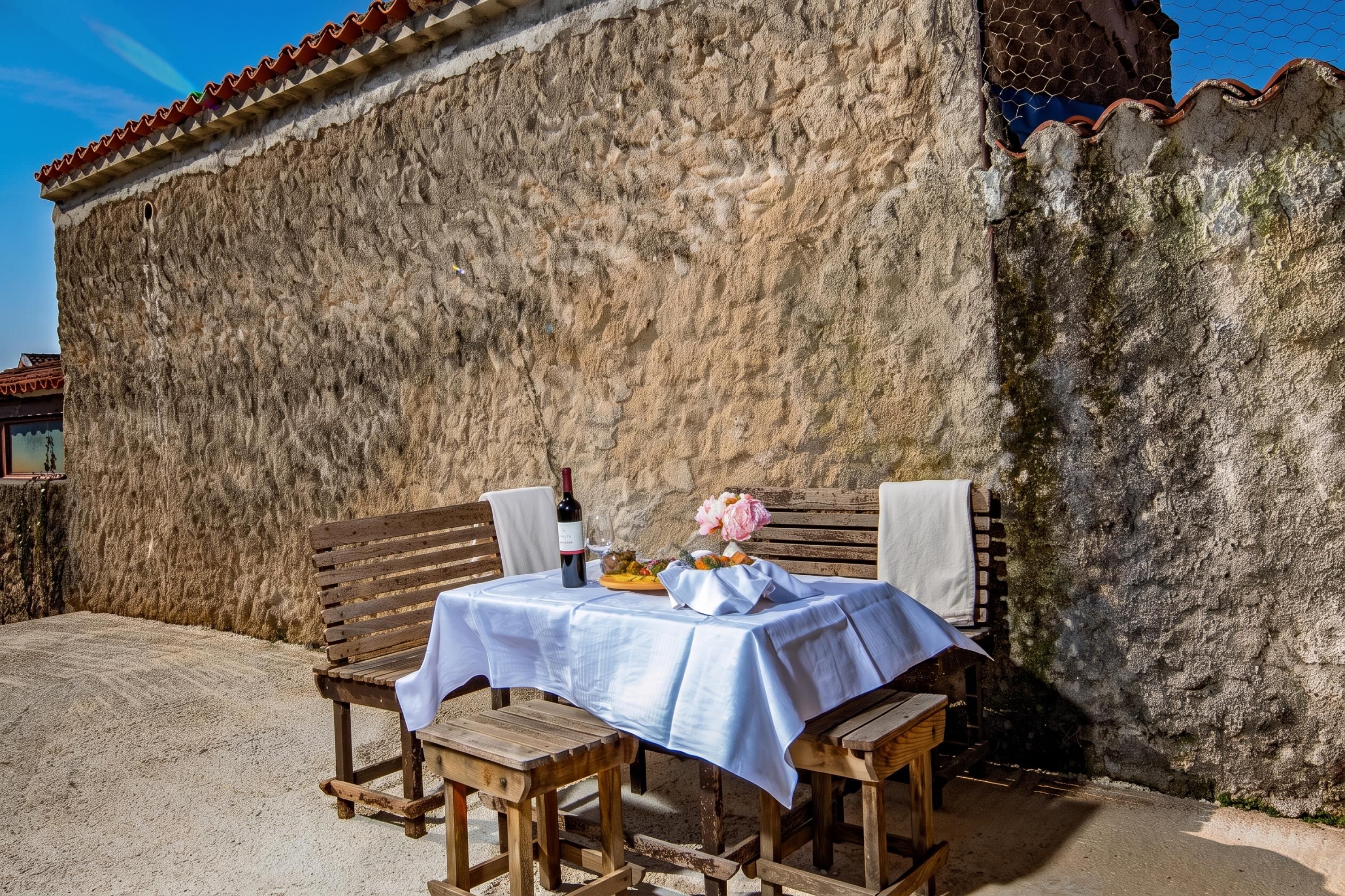 A table set outdoors with a bottle and flowers, against a stone wall.
