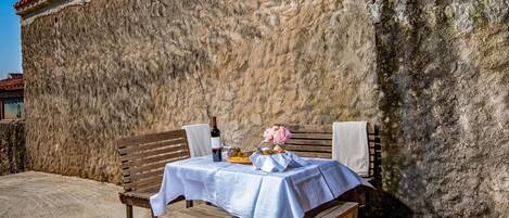 A table set outdoors with a bottle and flowers, against a stone wall.