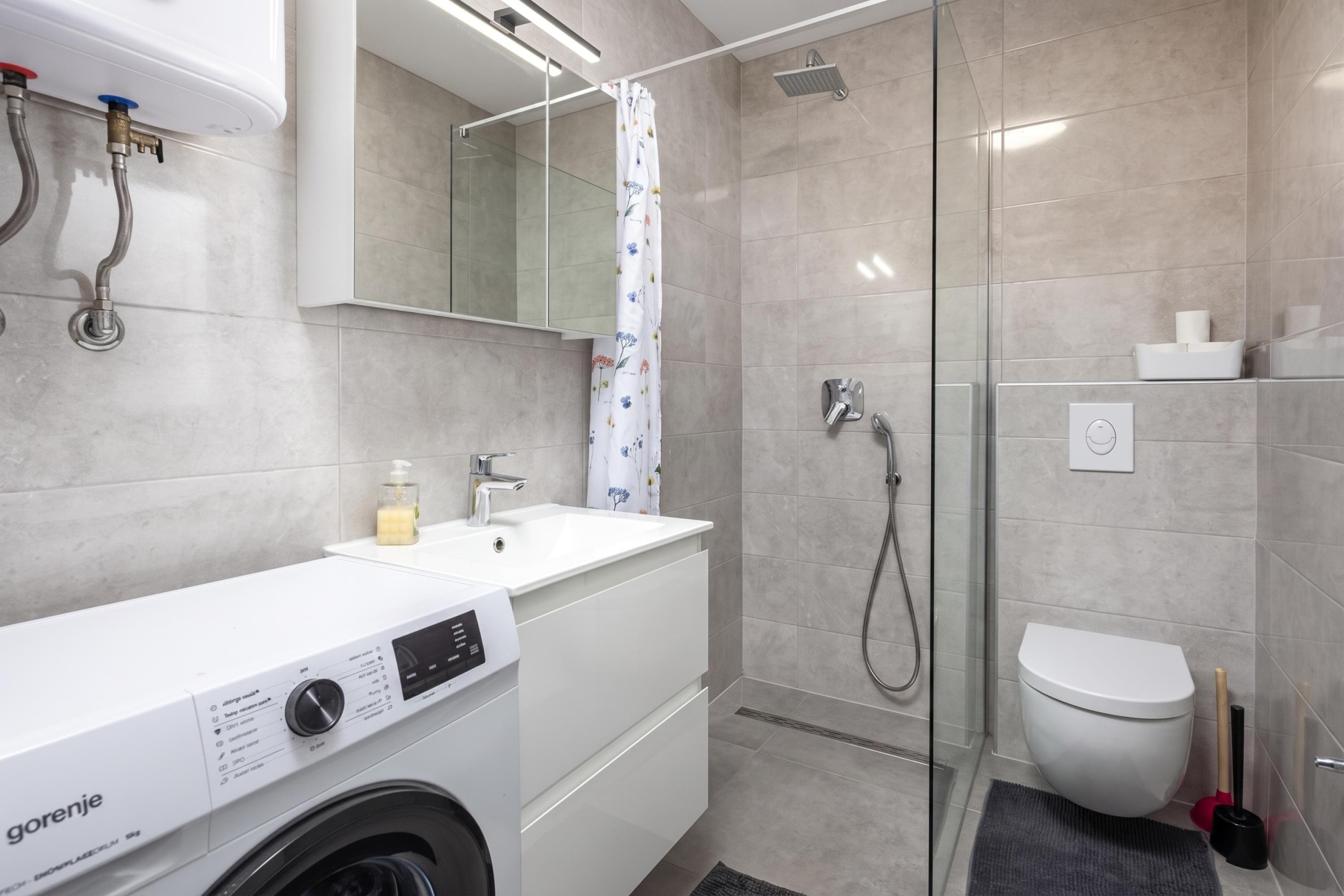 A modern bathroom with a washing machine, a sink, a toilet, and a shower area.