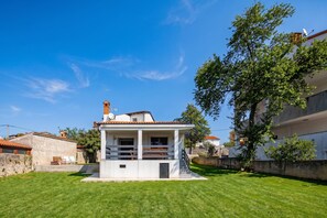 Un petit bâtiment blanc doté d’un balcon, entouré d’une pelouse bien entretenue et d’un arbre.