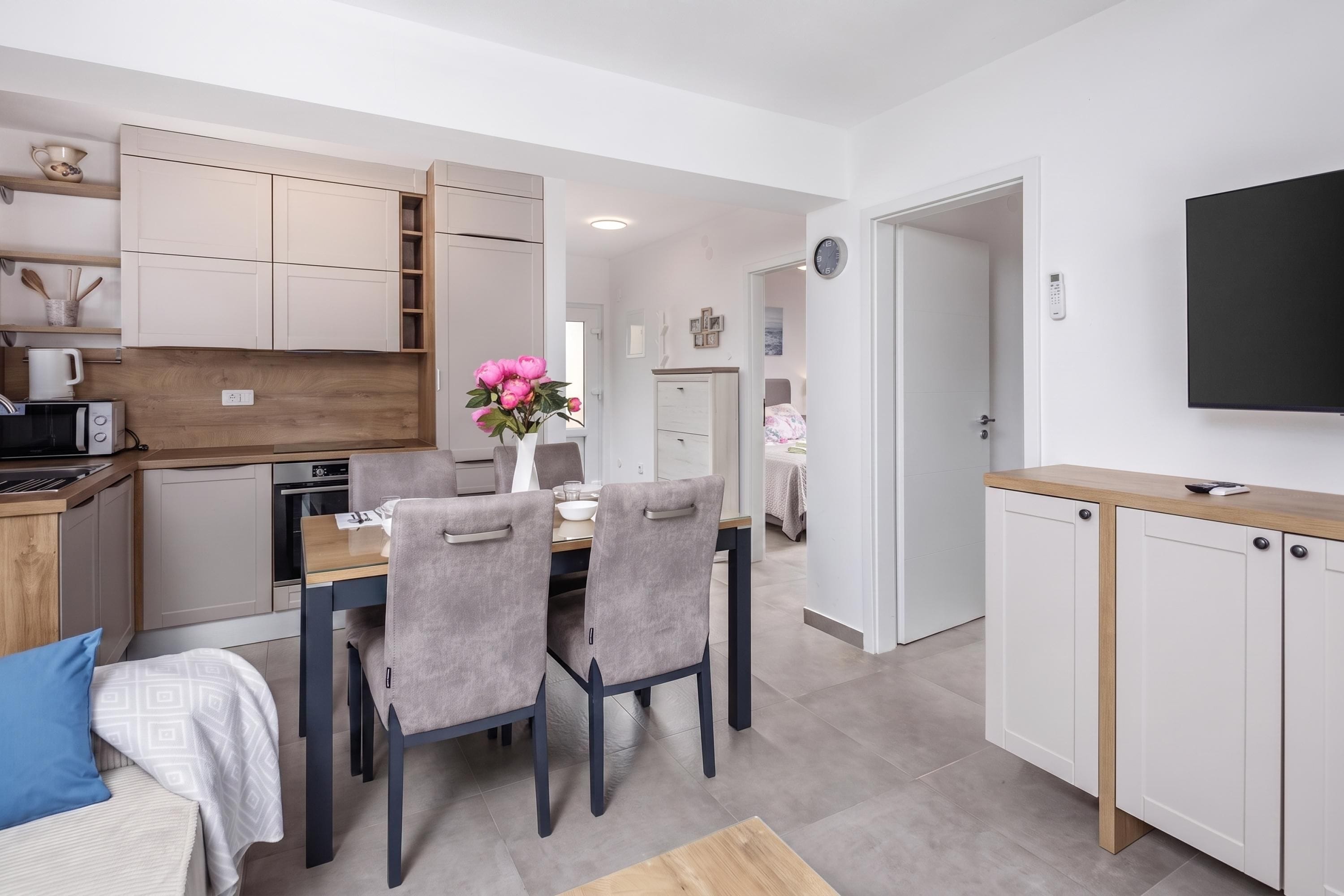 A modern kitchen with white cabinets, a dining area with a table and chairs, and a living space with a bed and a TV.
