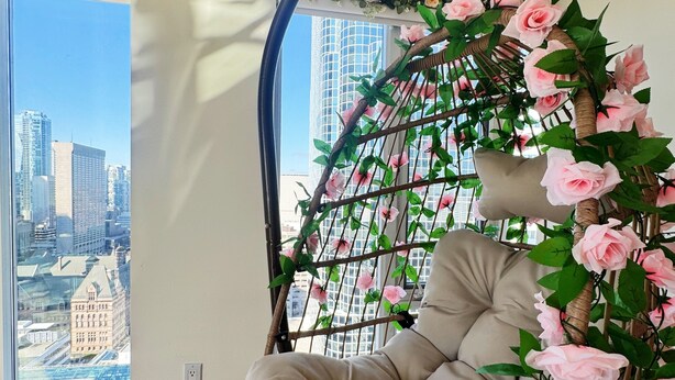 Una habitación con una silla colgante, un ventanal grande y vistas a un paisaje urbano.