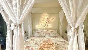 Una cama con dosel, una colcha estampada con motivos florales y una lámpara fijada a la pared.