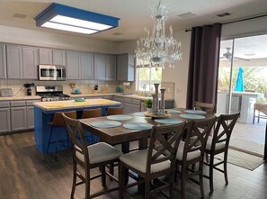 Une cuisine moderne avec des meubles gris, un îlot central, une table à manger avec des chaises et un lustre.