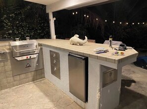 An outdoor kitchen with a built-in grill, a sink, and a refrigerator.