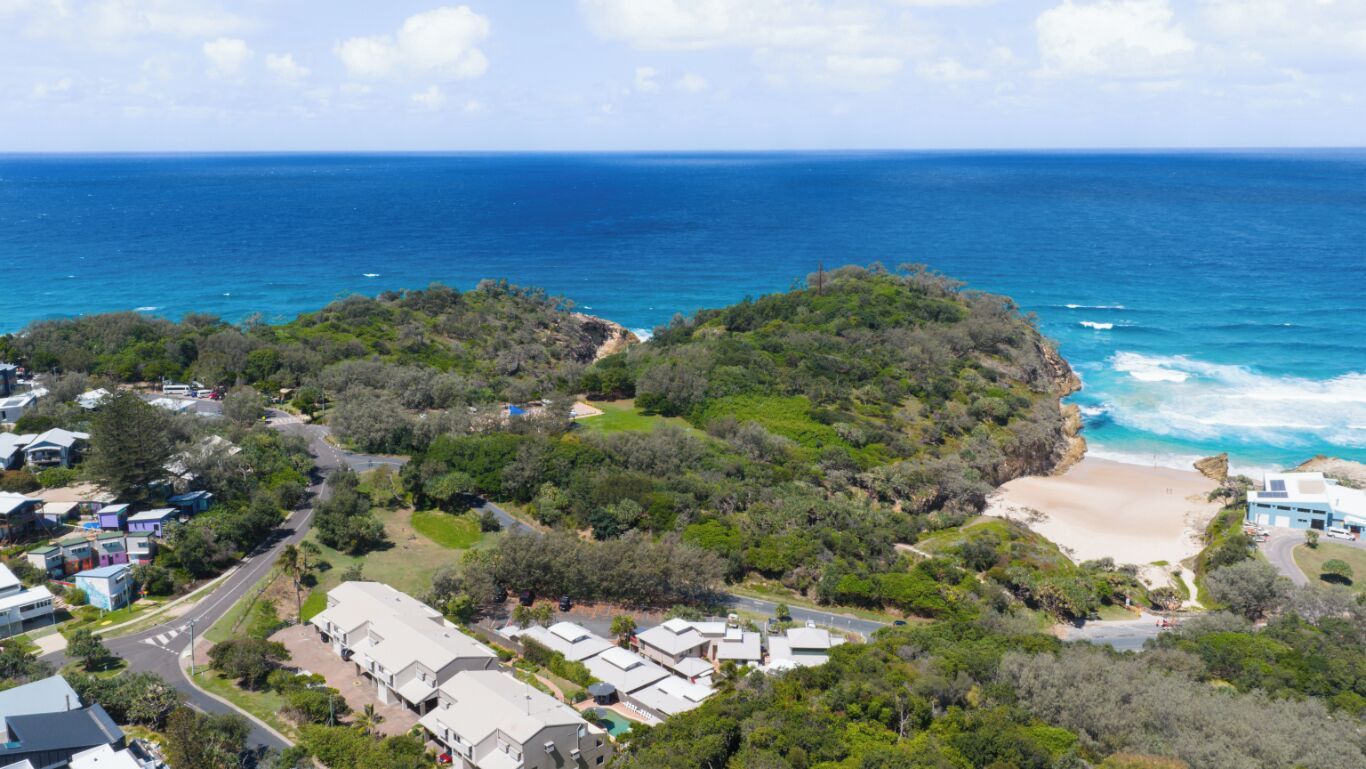 Vue aérienne d’une zone côtière comprenant une plage, une végétation luxuriante et des immeubles résidentiels.