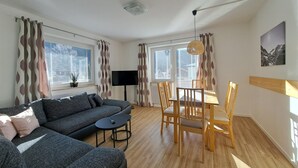 Una sala de estar moderna con un sofá, una mesa de comedor con sillas, un televisor y una lámpara de techo.
