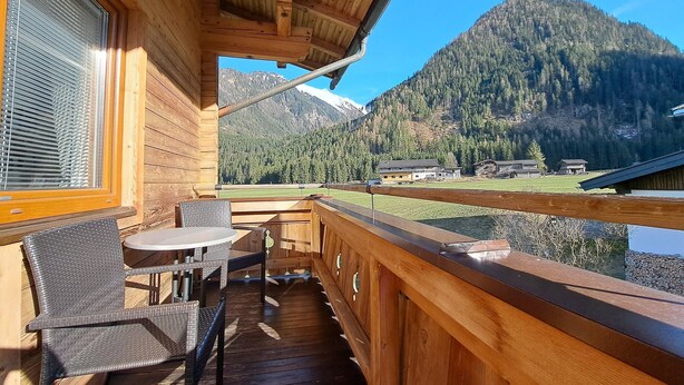 Una terraza de madera con una mesa y sillas, con vistas a un paisaje montañoso.