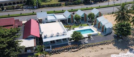 Un hotel frente a la playa con piscina, varias habitaciones y vistas al mar.