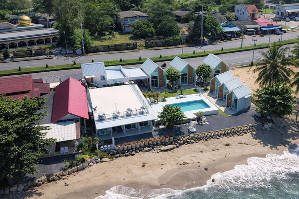 Un hotel frente a la playa con piscina, varias habitaciones y vistas al mar.