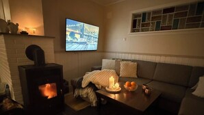 Ein gemütliches Wohnzimmer mit Kamin, einer Couch, einem Couchtisch mit Kerzen und einem an der Wand befestigten Fernseher.