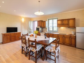 Una cocina amplia con armarios de madera, una mesa de comedor con sillas, un televisor y una ventana con cortinas.