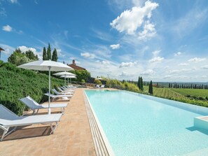 A poolside area with lounge chairs and umbrellas, a clear sky, and a view of the countryside. - Podere Galieni by Interhome (Certaldo)
