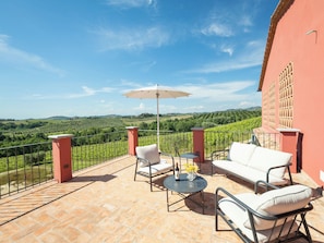 Une terrasse avec du mobilier d’extérieur, une table avec une bouteille et des verres, et une vue sur les vignes.