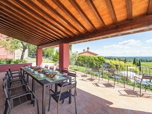 An outdoor patio with a table set for dining, surrounded by chairs, and a view of vineyards in the background. - Podere Galieni by Interhome (Certaldo)
