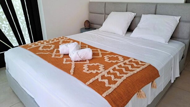 A neatly made bed with white linens and a brown patterned throw, two white pillows, and a nightstand with a decorative item. - Au Bois Dormant - 3 bedroom villa, swimming pool 10 minutes from the beach (Saint-Pierre)