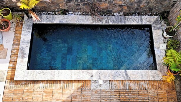 Una piscina rectangular con un muro de piedra y una terraza de madera.