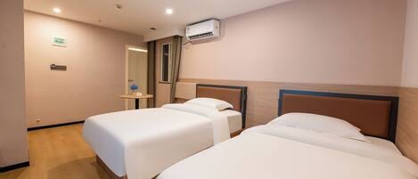 A hotel room with two single beds, a bedside table, an air conditioning unit, and a mirror.