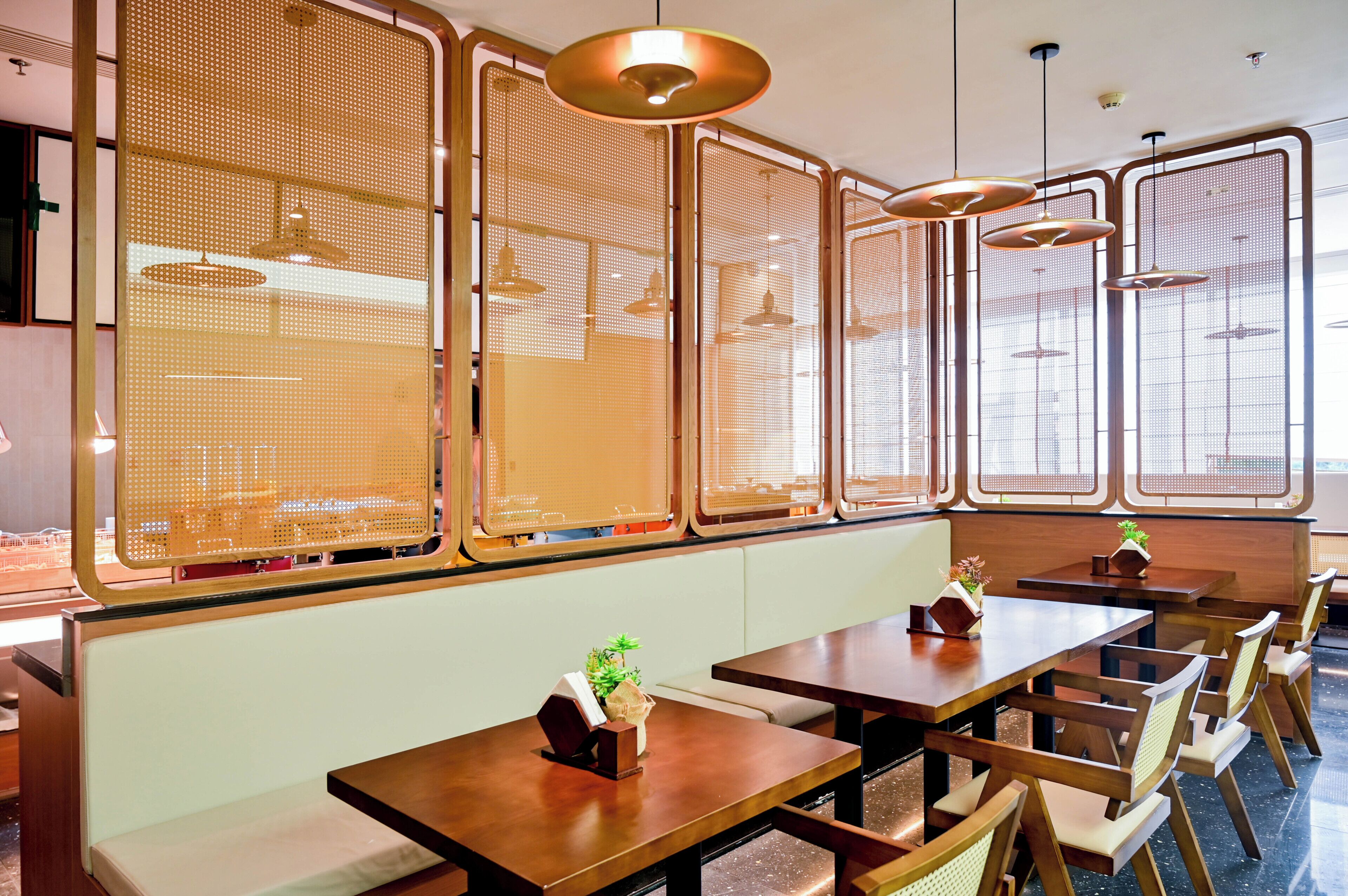 A restaurant interior with wooden tables, chairs, and a decorative partition with a perforated design.