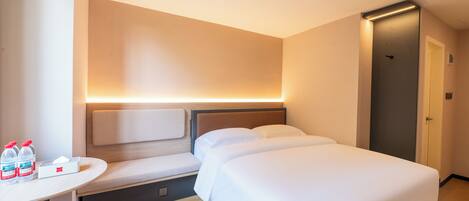 A hotel room with a bed, bedside table, and a bench. There are two bottles of water and a tissue box on the table.