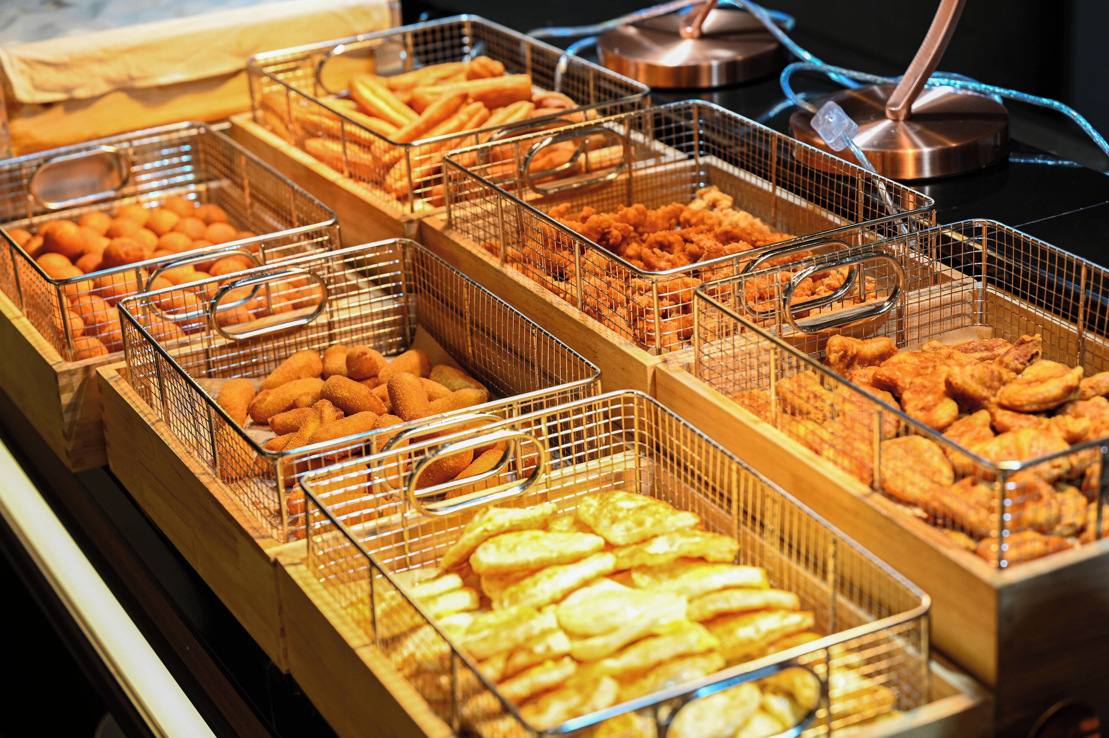 A buffet with various fried foods in wire baskets.