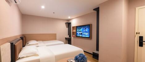 A hotel room with two beds, a round table with a vase of flowers, a mounted TV, and a wardrobe.