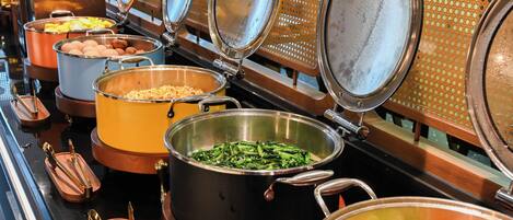A buffet with various food items in large pots, arranged on a counter with metal serving utensils.