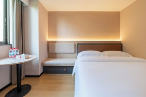 A hotel room with a bed, bedside table, and a window with curtains.