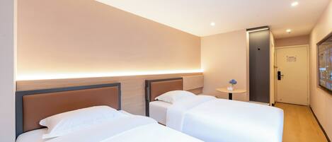 A hotel room with two beds, a small table, and a door leading to a bathroom.