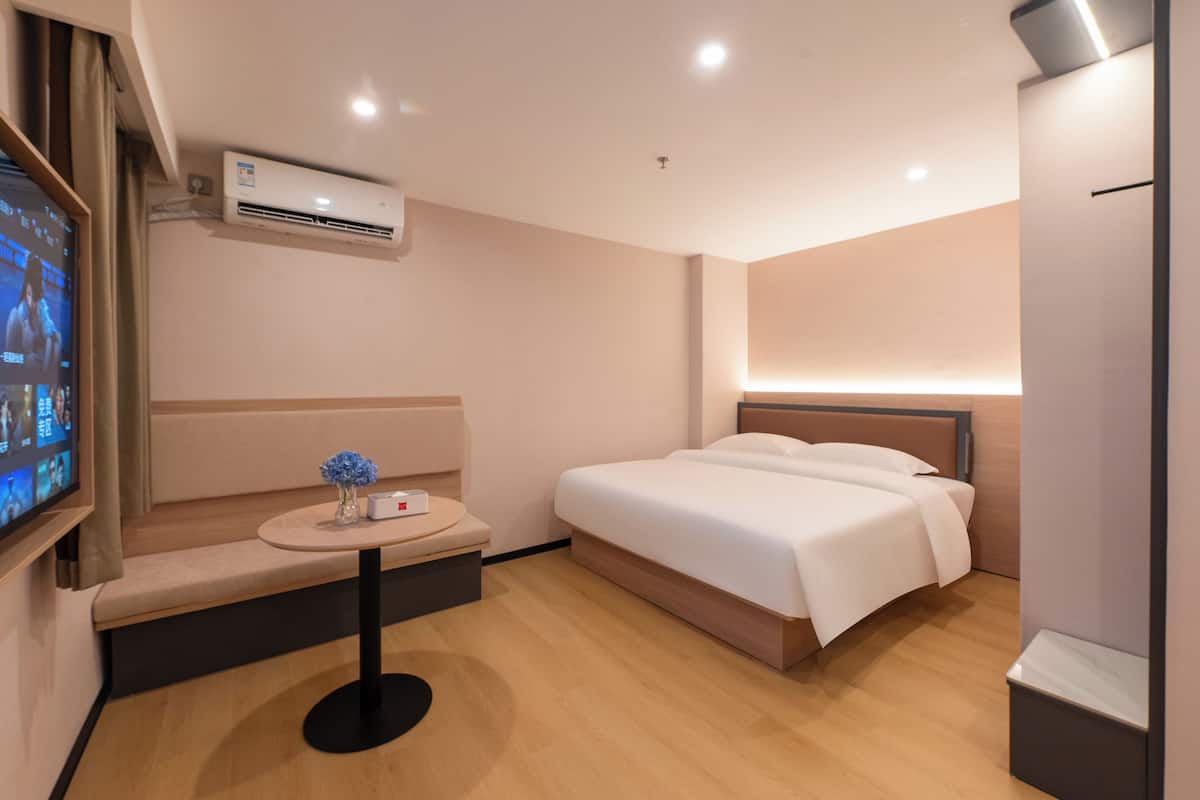 Ein Hotelzimmer mit einem Bett, einem kleinen Tisch mit einer Vase, einer Klimaanlage und einem Fernseher an der Wand.