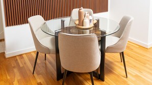 A modern dining area with a round glass table, four chairs, and a wooden slat wall. - Happiness at NO-CHARGE in walkaway Akard Travelbae Luxe Haus (Dallas)