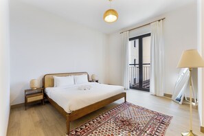 Un dormitorio ordenado con una cama de madera, una lámpara de noche, una mesita con lámpara y una alfombra estampada.