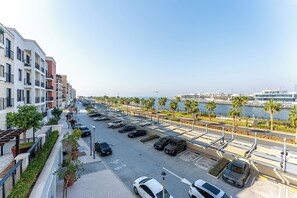 Un espace de stationnement où sont garées plusieurs voitures, avec vue sur le front de mer et bordé d’une rangée d’immeubles modernes.