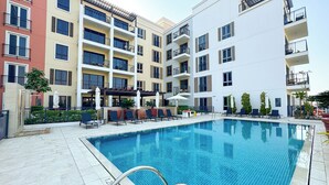 Piscina rodeada por edifícios altos com varandas, área de estar ao ar livre e plantas em vasos.
