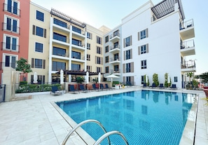 Une piscine entourée d’immeubles à plusieurs étages, dotés de balcons, de coins salon extérieurs et de plantes en pot.