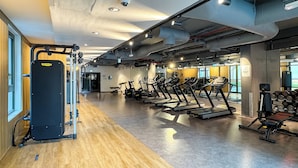 Academia com equipamentos de cardio, aparelhos de musculação e piso de madeira.