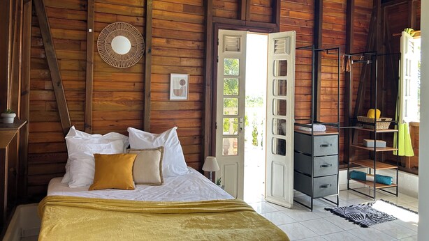 Un dormitorio de cabaña de madera con cama, cómoda y puerta abierta a un balcón.