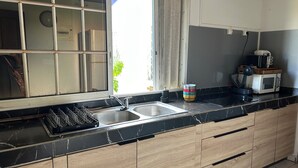 Una cocina con encimera de mármol negro, pileta de acero inoxidable, armarios de madera y una ventana con vistas a zonas verdes.
